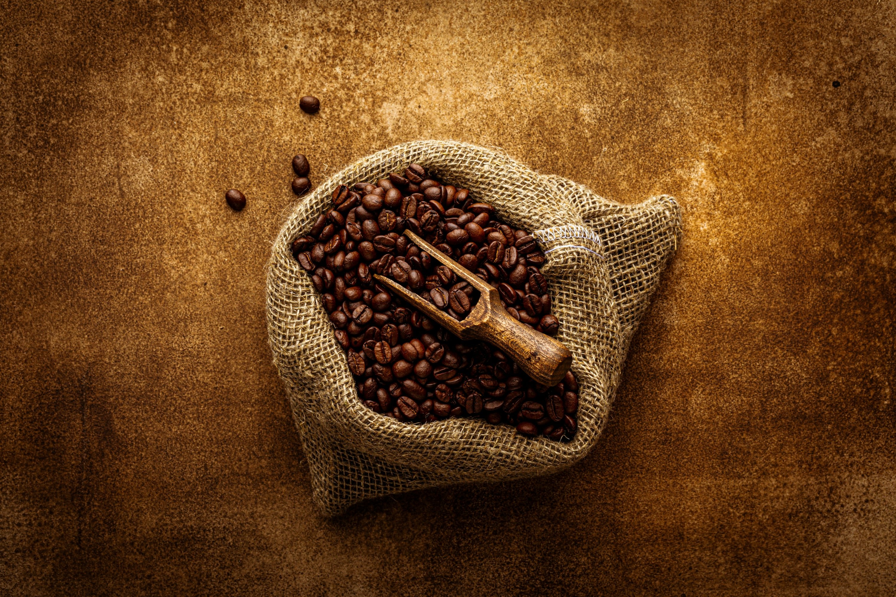 Flat-lay of roasted coffee beans spilling from a vintage burlap coffee sack, overhead view