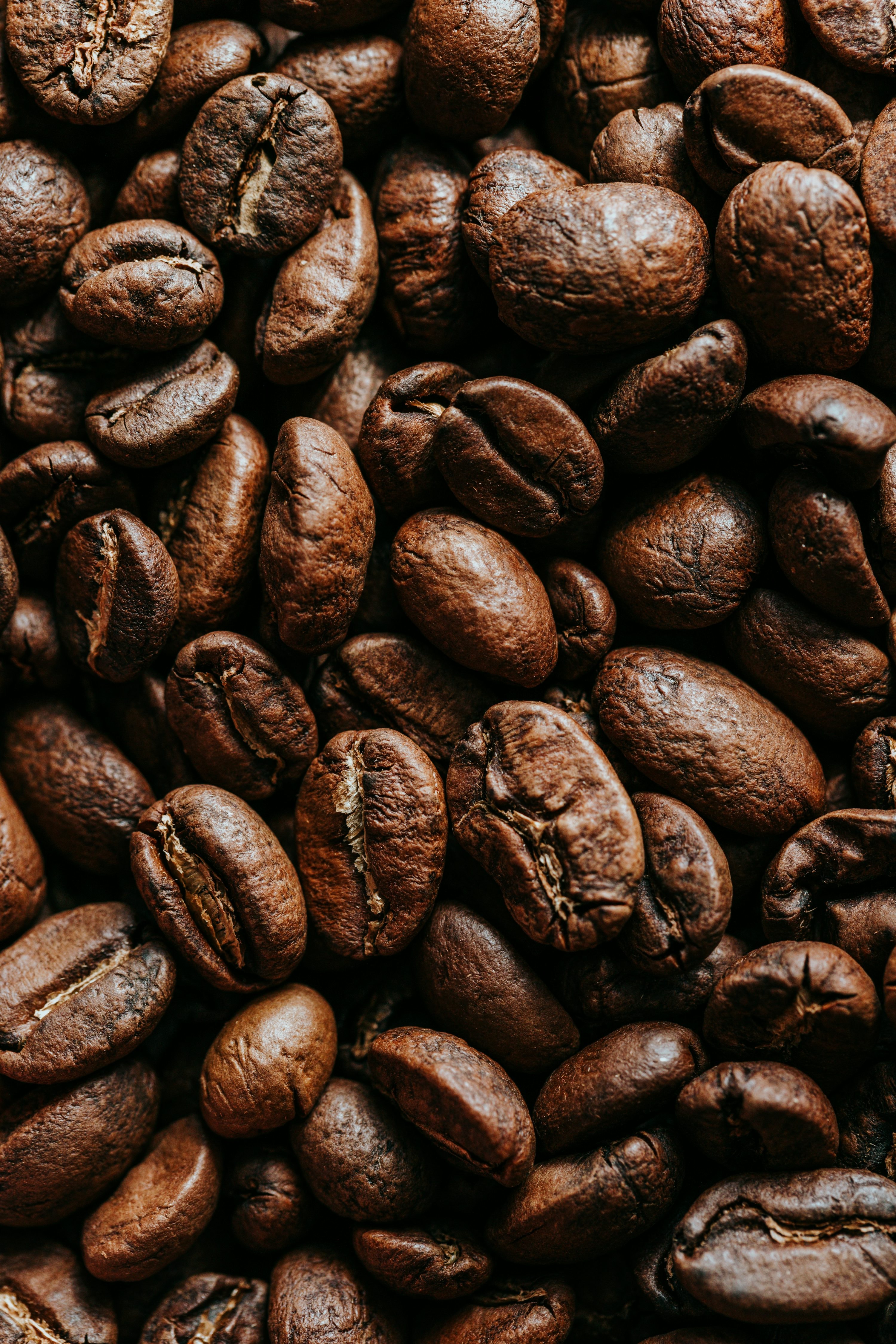 Medium-roast coffee beans scattered across a matching brown wooden surface, overhead texture shot