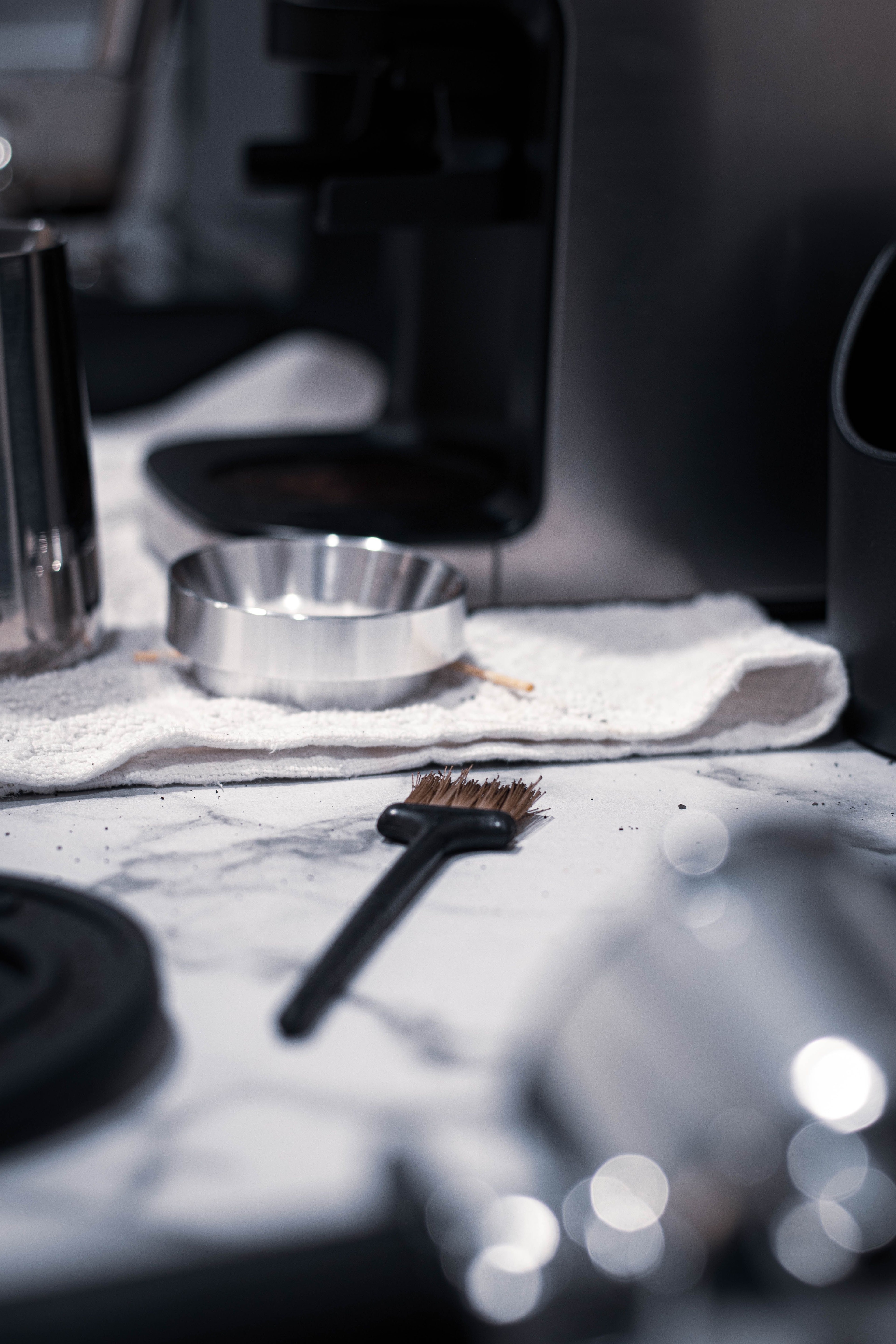 Coffee tools and a cleaning brush arranged on a marble counter, barista maintenance kit