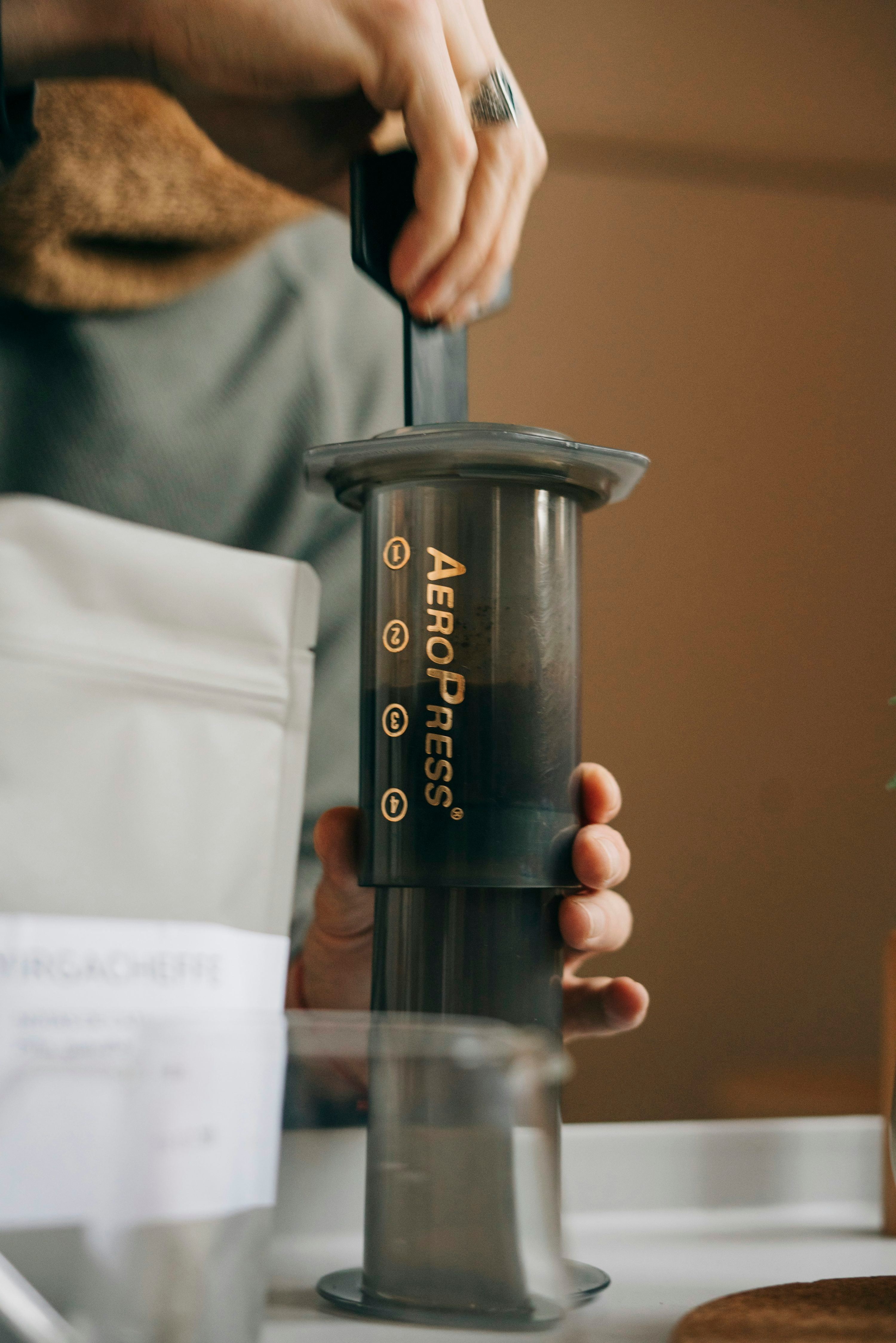 Person holding a black and silver AeroPress-style immersion coffee brewer
