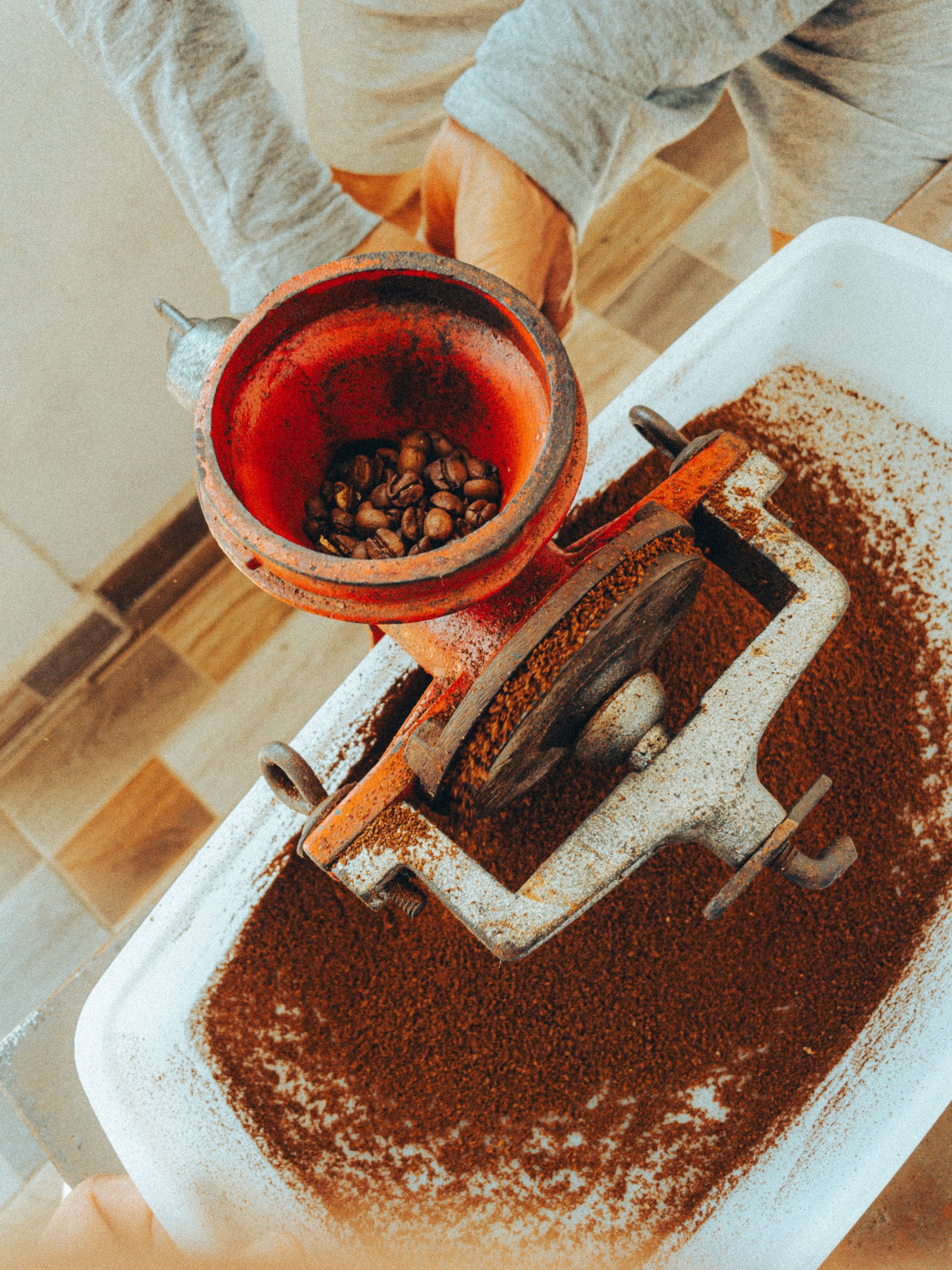 Rustic manual hand-crank coffee grinder with fresh coffee beans and grounds, top view