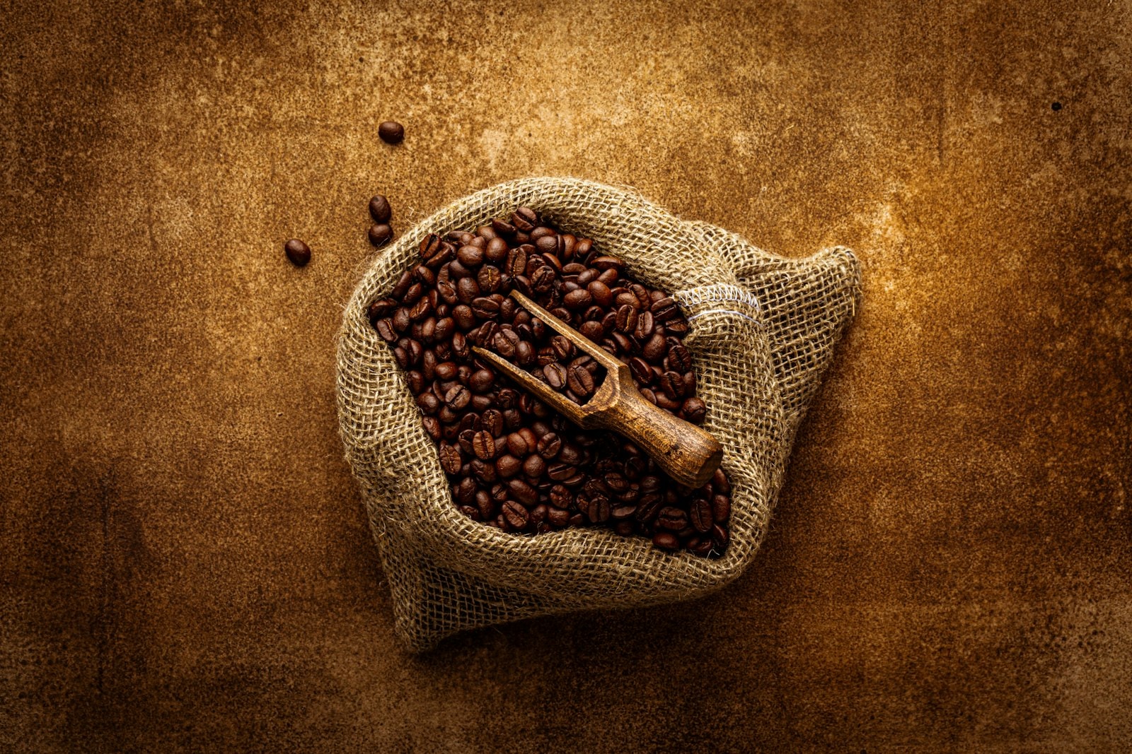 Roasted coffee beans spilling from a rustic burlap sack with a metal scoop, styled lifestyle shot