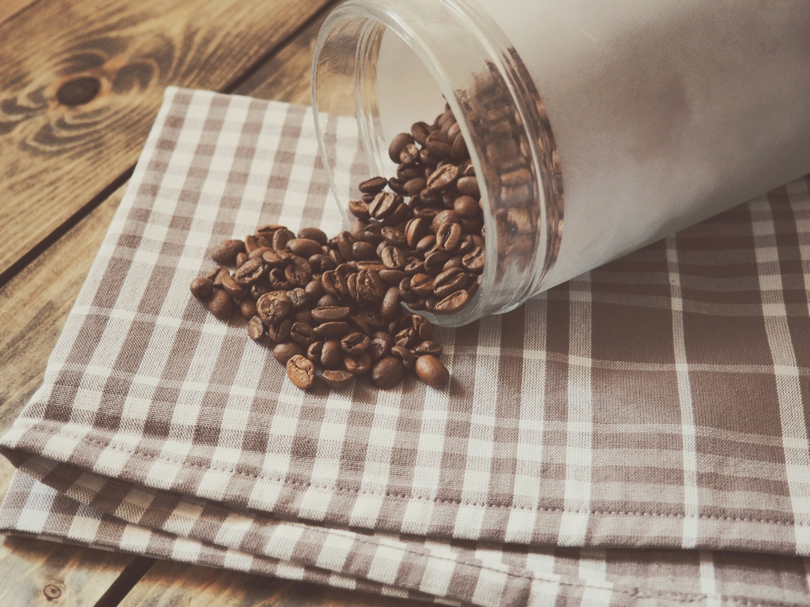 A glass jar of roasted coffee beans on a wooden surface, home storage scene