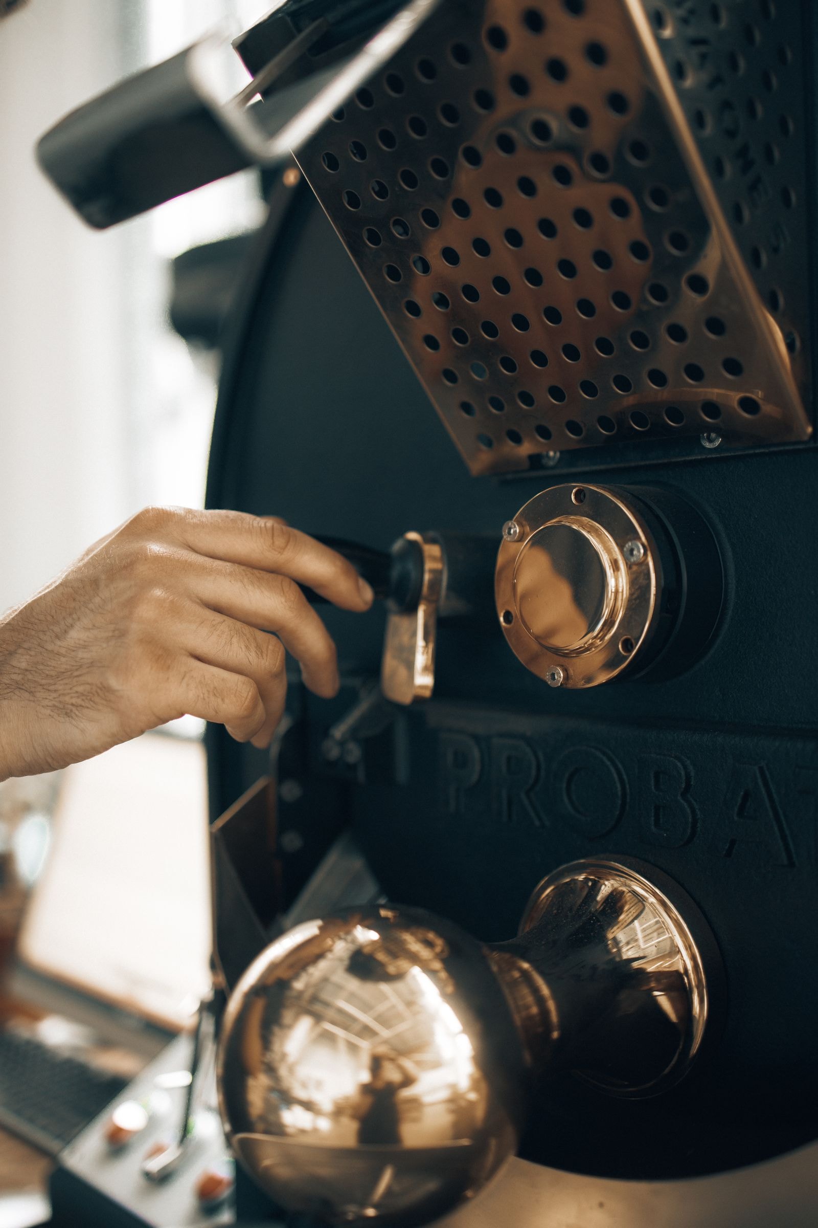 Close-up of a hand adjusting controls on an industrial coffee roasting machine